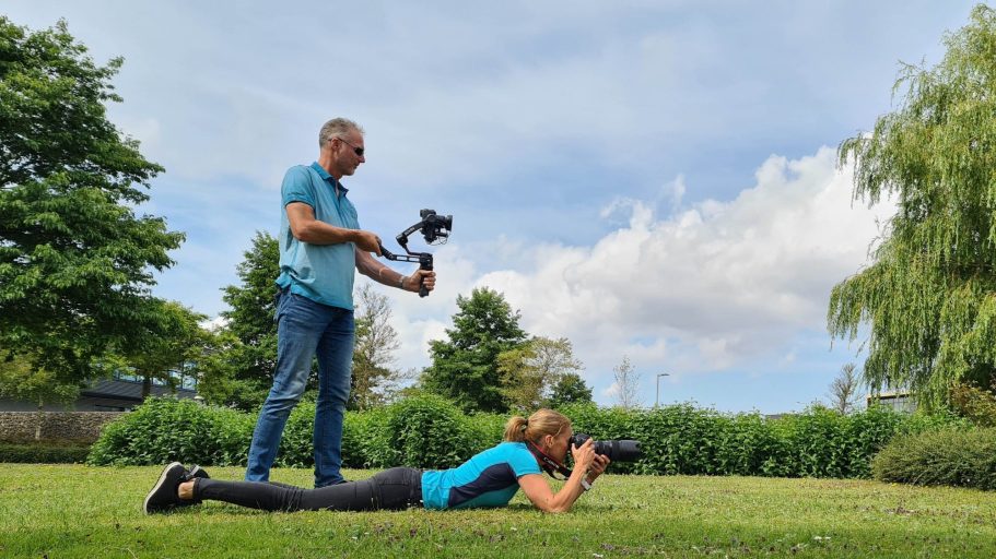 Een man houdt een camera vast terwijl een vrouw op de grond foto's maakt.