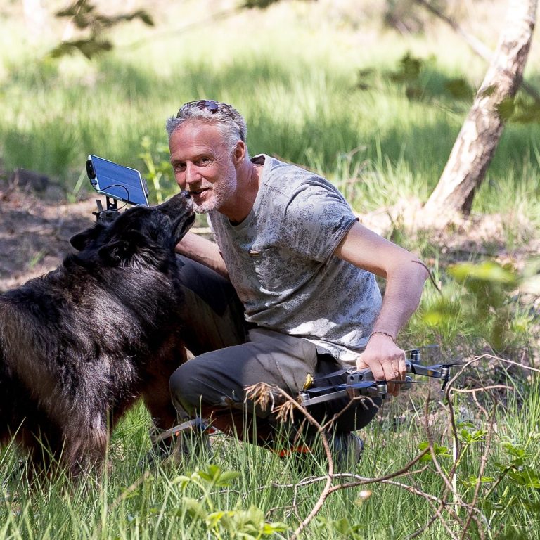 Een man knielt in het gras terwijl zijn hond hem enthousiast begroet.