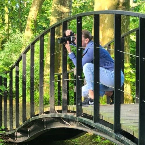 Fotograaf zit op een brug en maakt een foto in een groene omgeving.