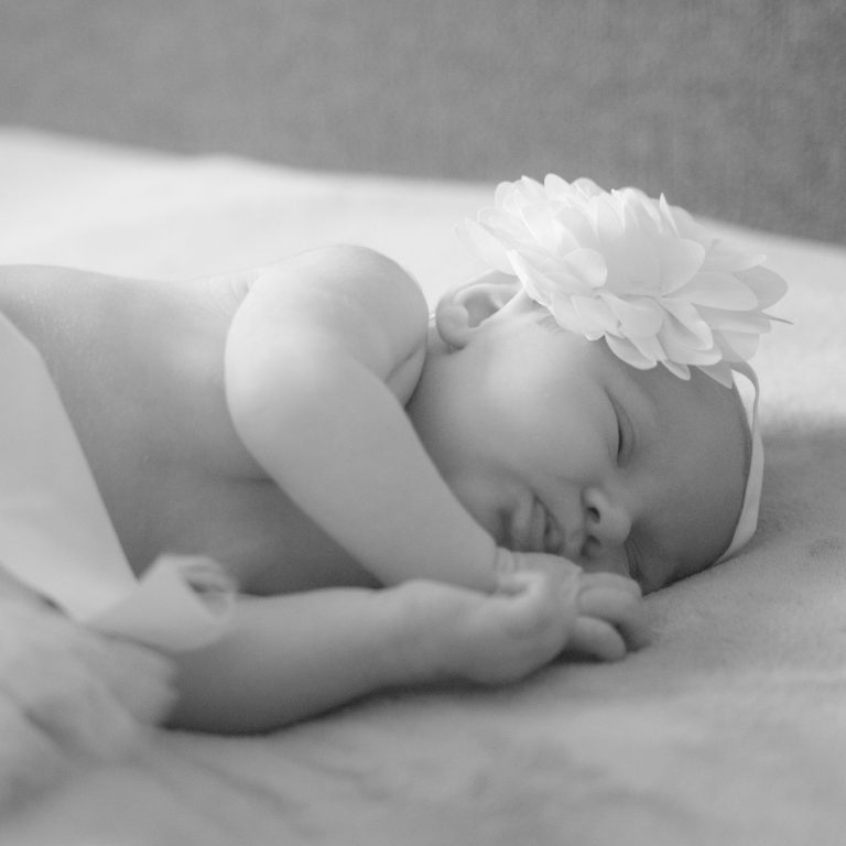 Slapende baby met een grote witte bloem op haar hoofd, op een zachte ondergrond.