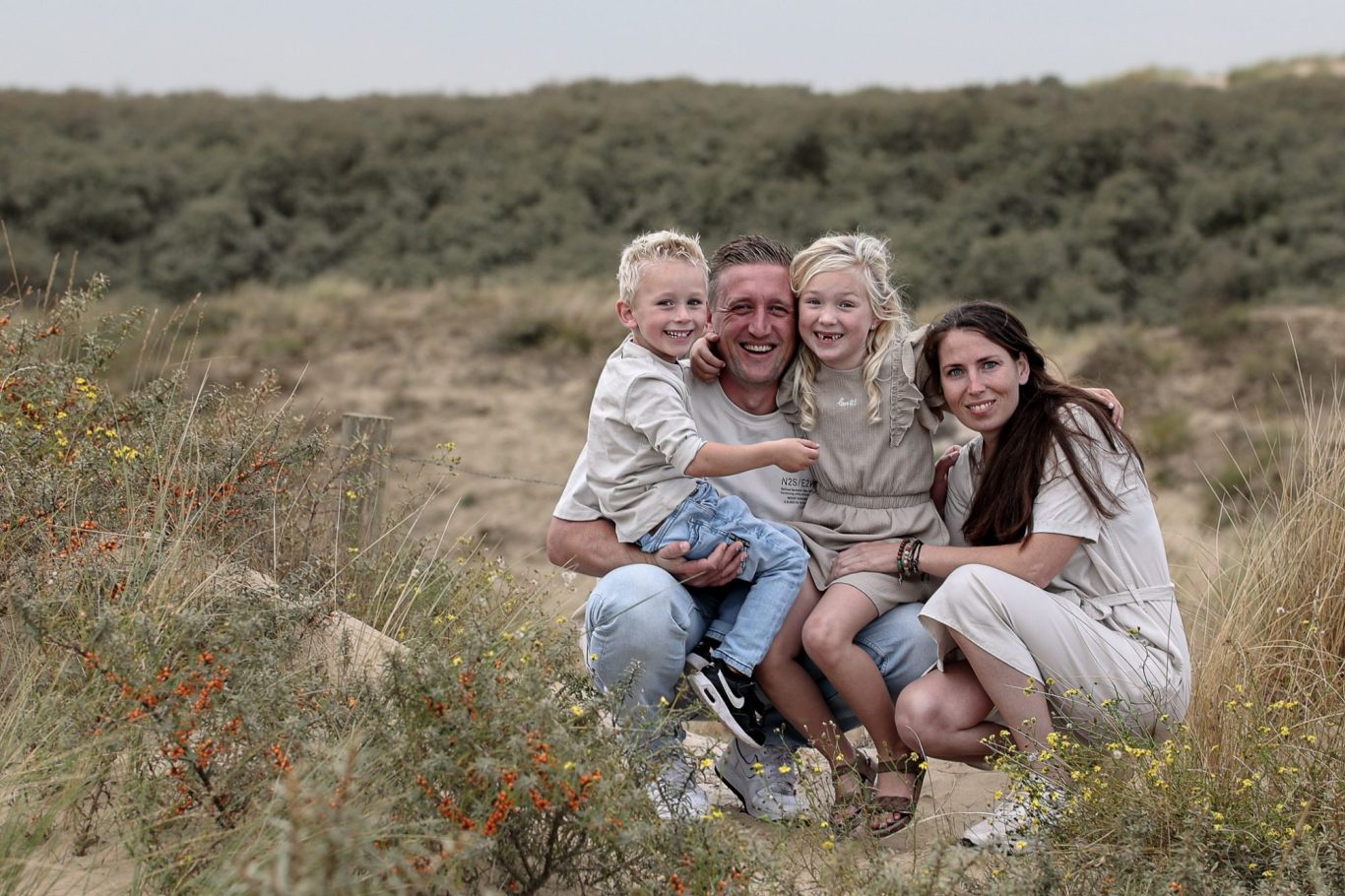 Een gezin bestaat uit twee volwassenen en twee kinderen, zittend in een groene, zandige omgeving.